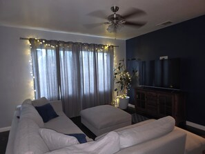 Ein Wohnzimmer mit Deckenventilator, einer Couch, einem Fernseher und einer Pflanze mit Beleuchtung.