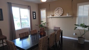 A dining room with a dark wooden table, wicker chairs, a wall clock, and potted plants. - Spacious 4-bedroom house in lovely Bakersfield with AC (Bakersfield)