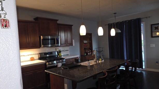 A modern kitchen with dark wood cabinets, stainless steel appliances, and pendant lighting. - Spacious 4-bedroom house in lovely Bakersfield with AC (Bakersfield)