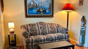 Un salon avec un canapé à motifs, une table basse, une lampe, un tableau et une statue.