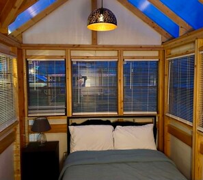Ein Schlafzimmer mit einem Bett, einem Nachttisch, einer Lampe und einem Oberlicht.