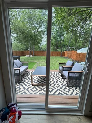 A sliding glass door leading to an outdoor patio with a patterned rug, two sofas, and a coffee table.
