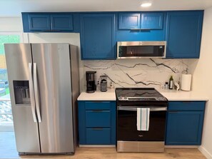 A modern kitchen with stainless steel appliances, blue cabinets, and a marble backsplash.