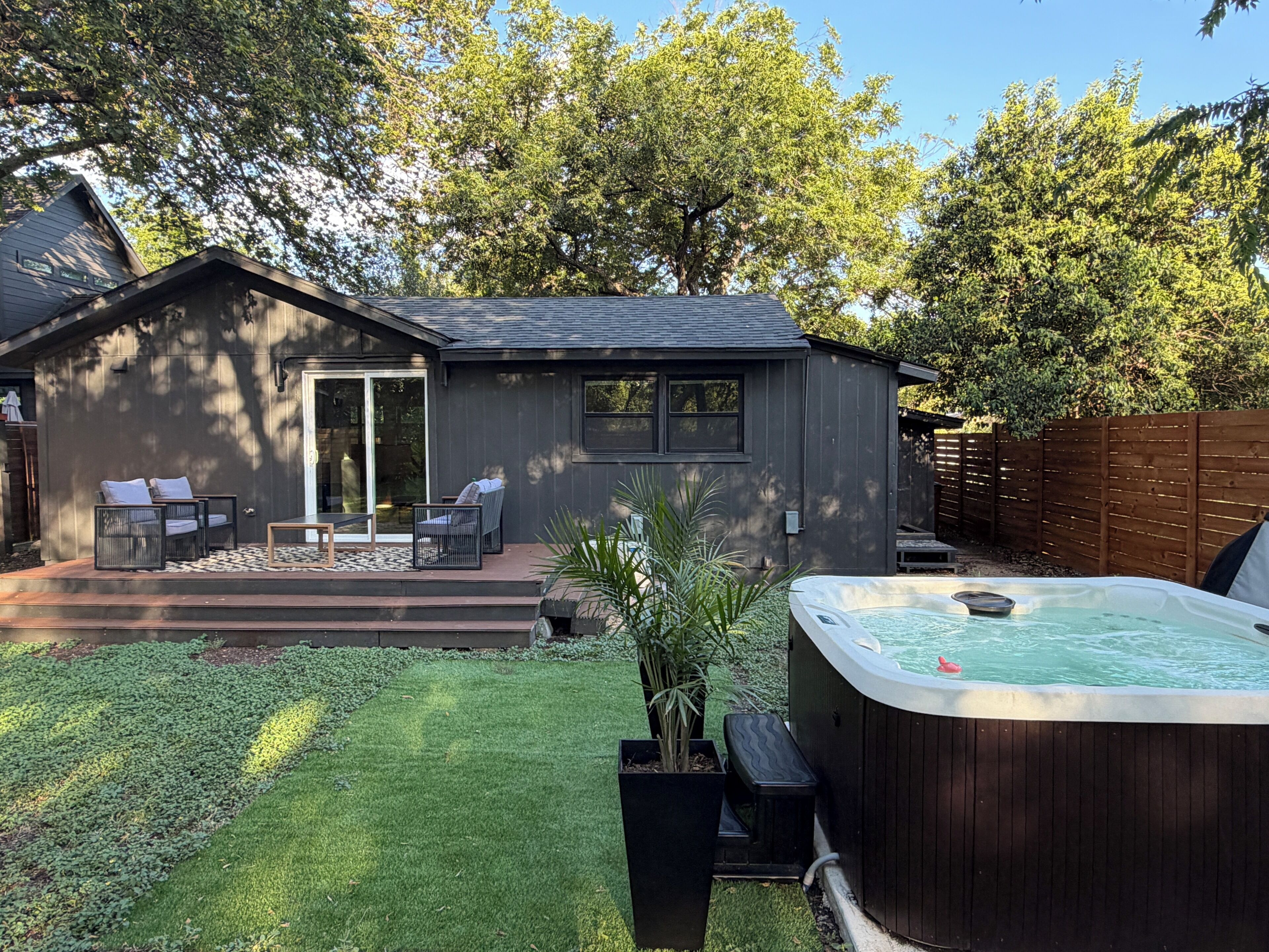 Un jardin avec un jacuzzi, une terrasse couverte avec des chaises et une clôture en bois.