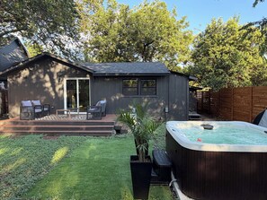 A backyard with a hot tub, a covered patio with chairs, and a wooden fence. - Modern Austin Retreat with Hot Tub & Outdoor Shower (Austin)