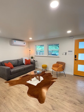 A modern living room with a grey sofa, a round glass coffee table, a brown leather rug, and a yellow chair.