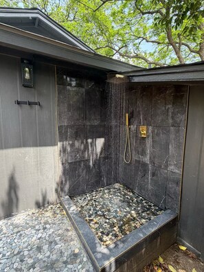 A stone shower enclosure with a built-in seating area and a handheld showerhead. - Modern Austin Retreat with Hot Tub & Outdoor Shower (Austin)