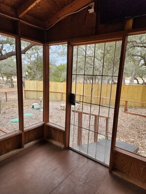 Habitación con paredes de madera y un ventanal grande, con vistas a un espacio exterior con cerca de madera y árboles.