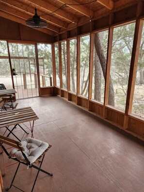 A spacious room with large windows, a wooden ceiling, and a table with chairs. - Jolly Ranch: Cozy 2-bdrm cabin in Spring Branch/Canyon Lake, Hill Country (Spring Branch)
