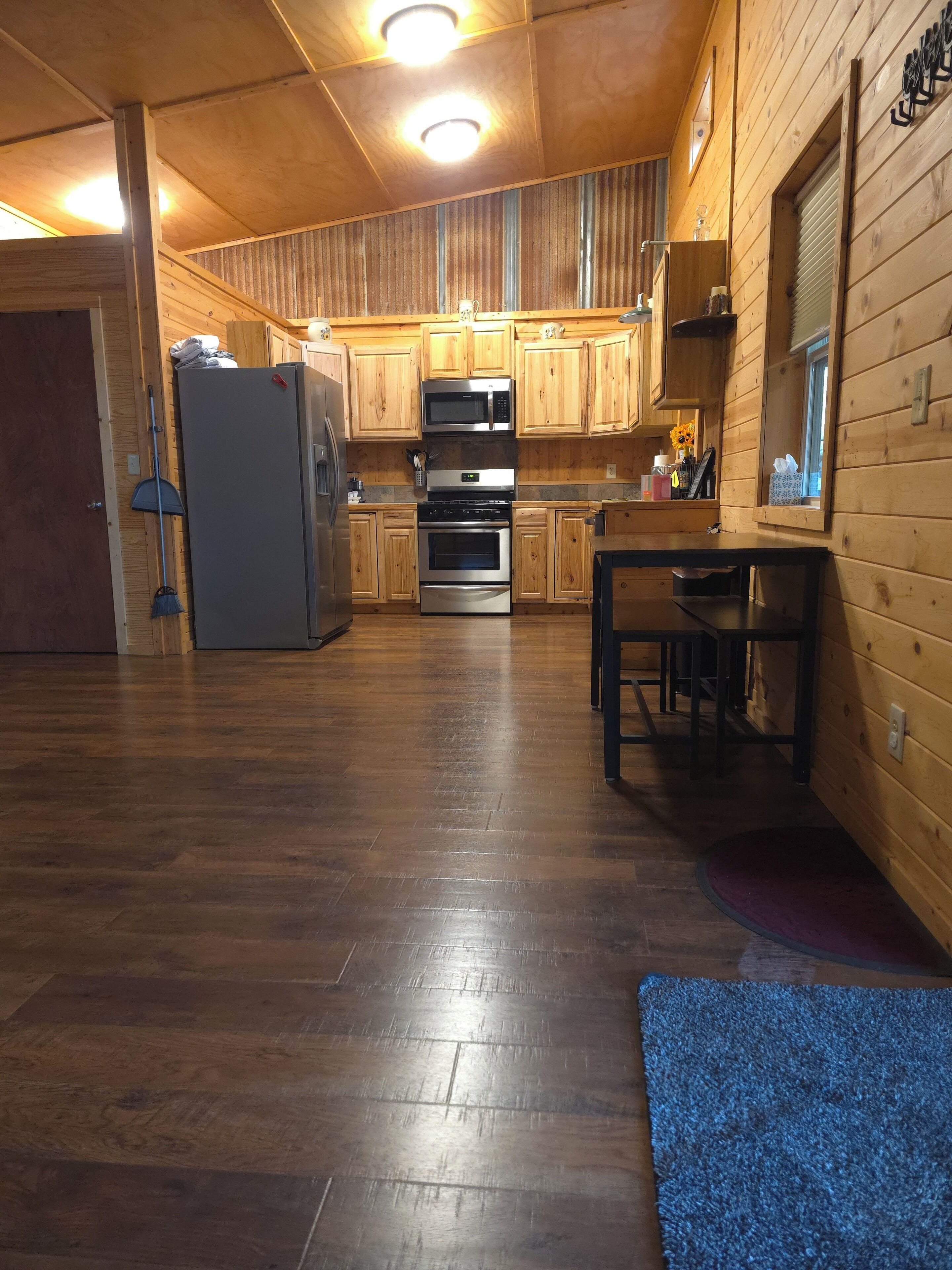 Un interior de madera con zona de cocina equipada con refrigerador, microondas y horno, además de una mesa de comedor con sillas.