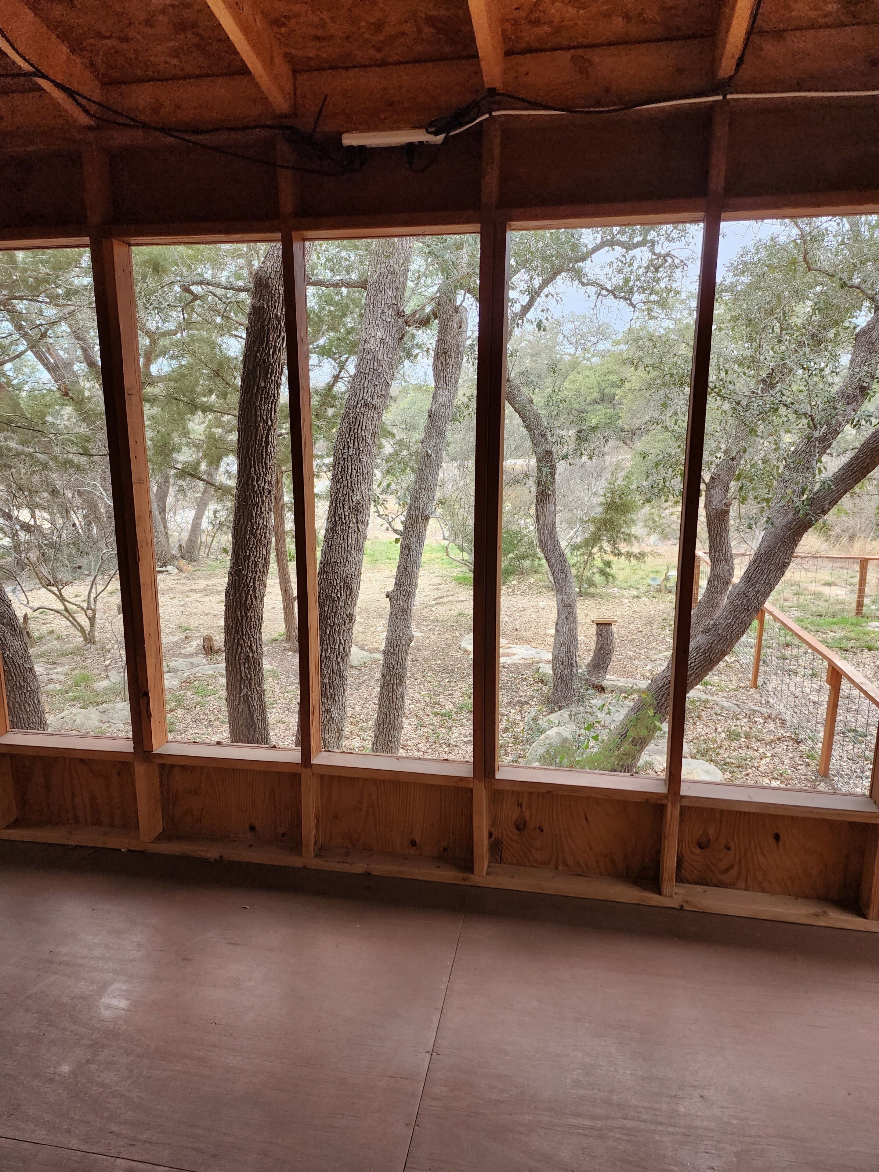 Habitació amb grans finestres, bigues de fusta i vista als arbres.