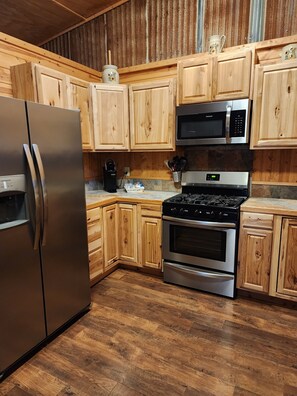 A kitchen with wooden cabinets, a stainless steel refrigerator, a microwave, and an oven. - Jolly Ranch: Cozy 2-bdrm cabin in Spring Branch/Canyon Lake, Hill Country (Spring Branch)