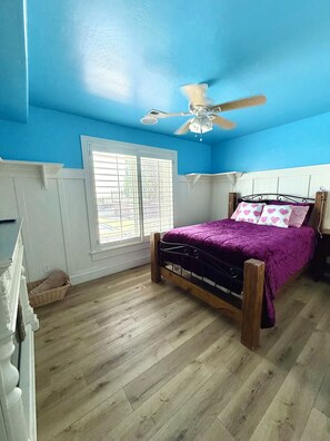 Un dormitorio con una cama de madera, un ventilador de techo y una ventana con persianas.