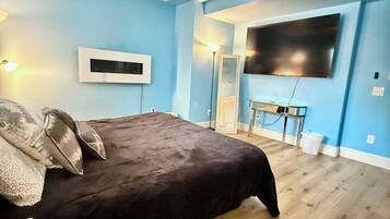 A bedroom with a bed, a ceiling fan, a TV, and a desk with a lamp.