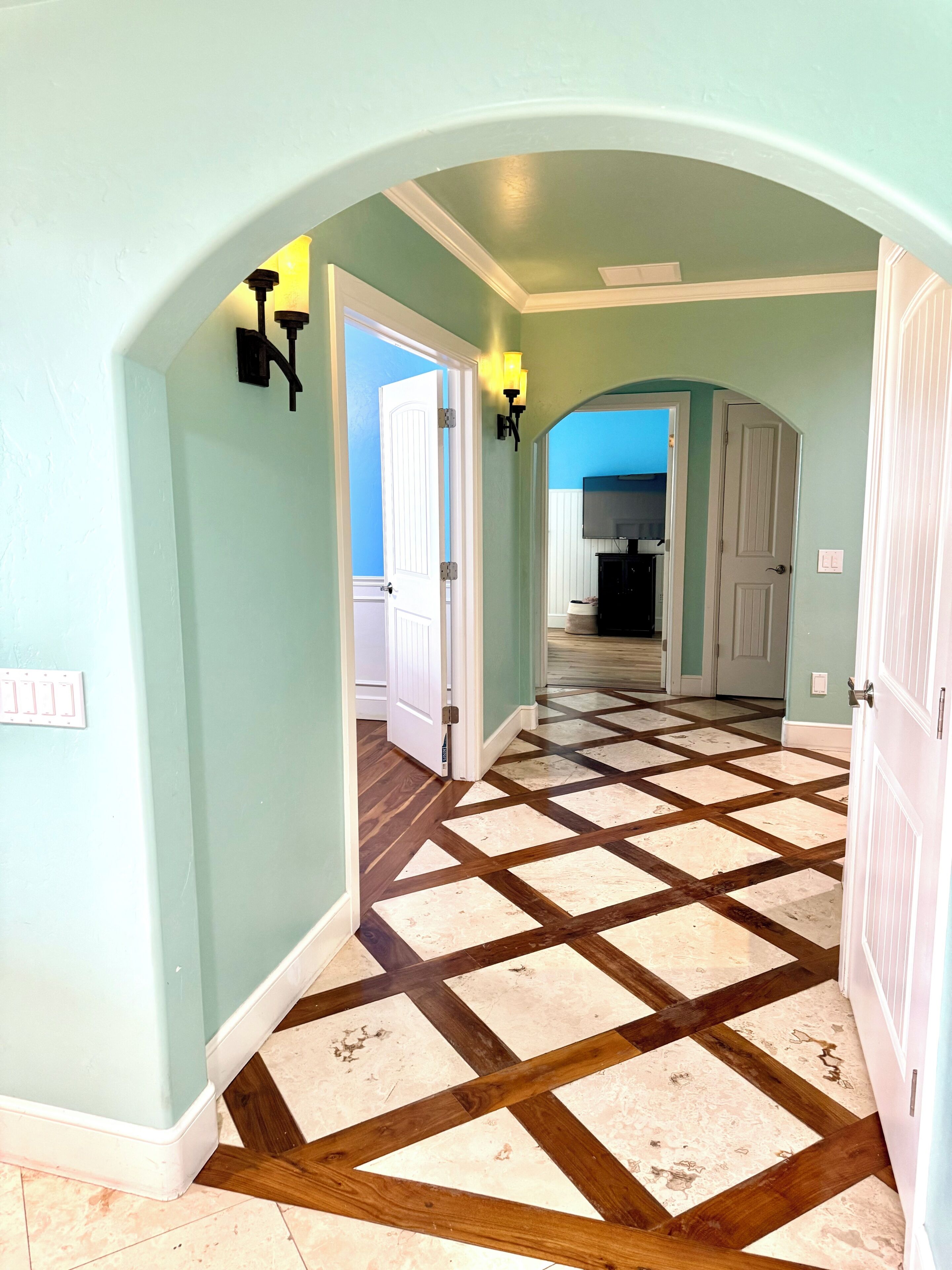 A hallway with a checkered floor pattern, light green walls, and a white door at the end.