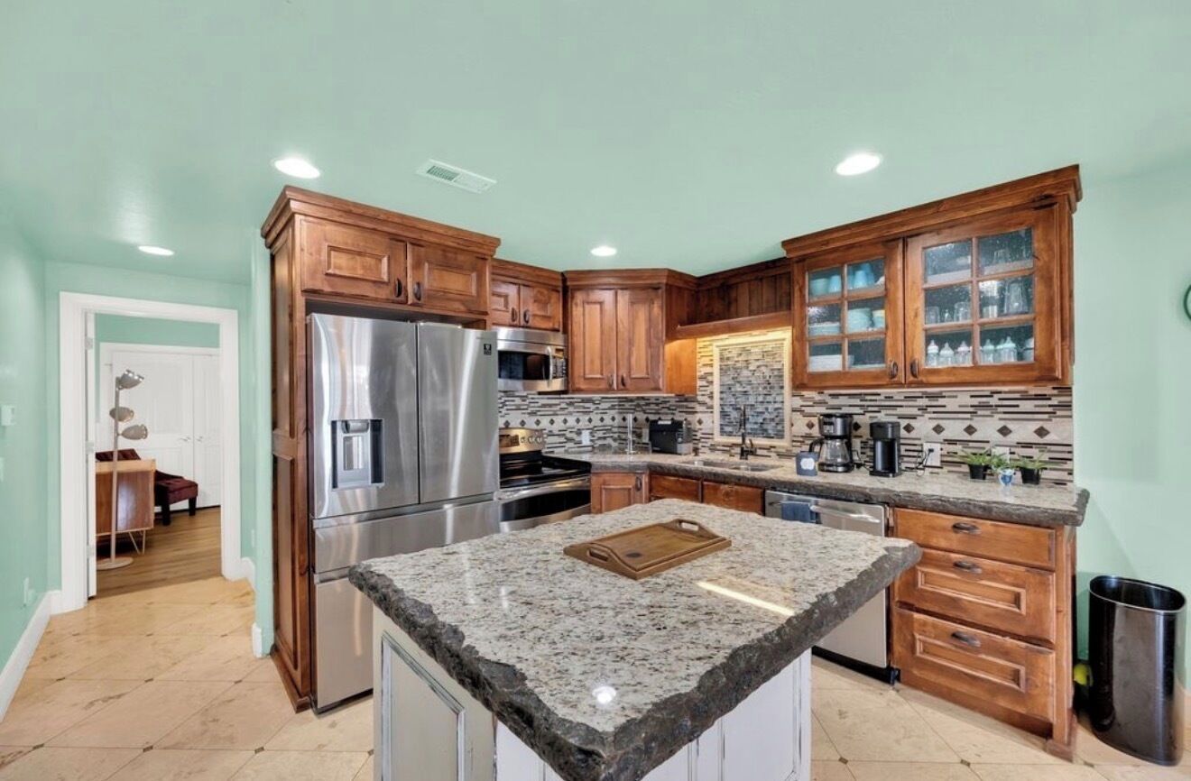 A kitchen with wooden cabinets, granite countertops, stainless steel appliances, and a backsplash.