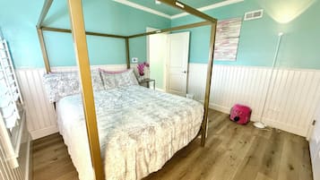 A four-poster bed with a canopy, a wooden floor, a white door, and a wall-mounted fan.