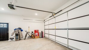 Eine Garage mit weißer Tür, einem Fahrrad, einem Ventilator und einer Kiste.