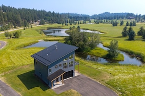 A modern two-story building with a flat roof, surrounded by a well-maintained lawn and a small pond. - New Riverfront Retreat Near Bigfork (Bigfork)
