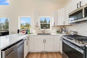 A modern kitchen with white cabinetry, a stainless steel range, and a window overlooking a forest.