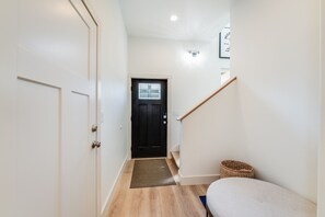 A narrow hallway with a wooden floor, a black door with a window, and a small rug at the entrance.