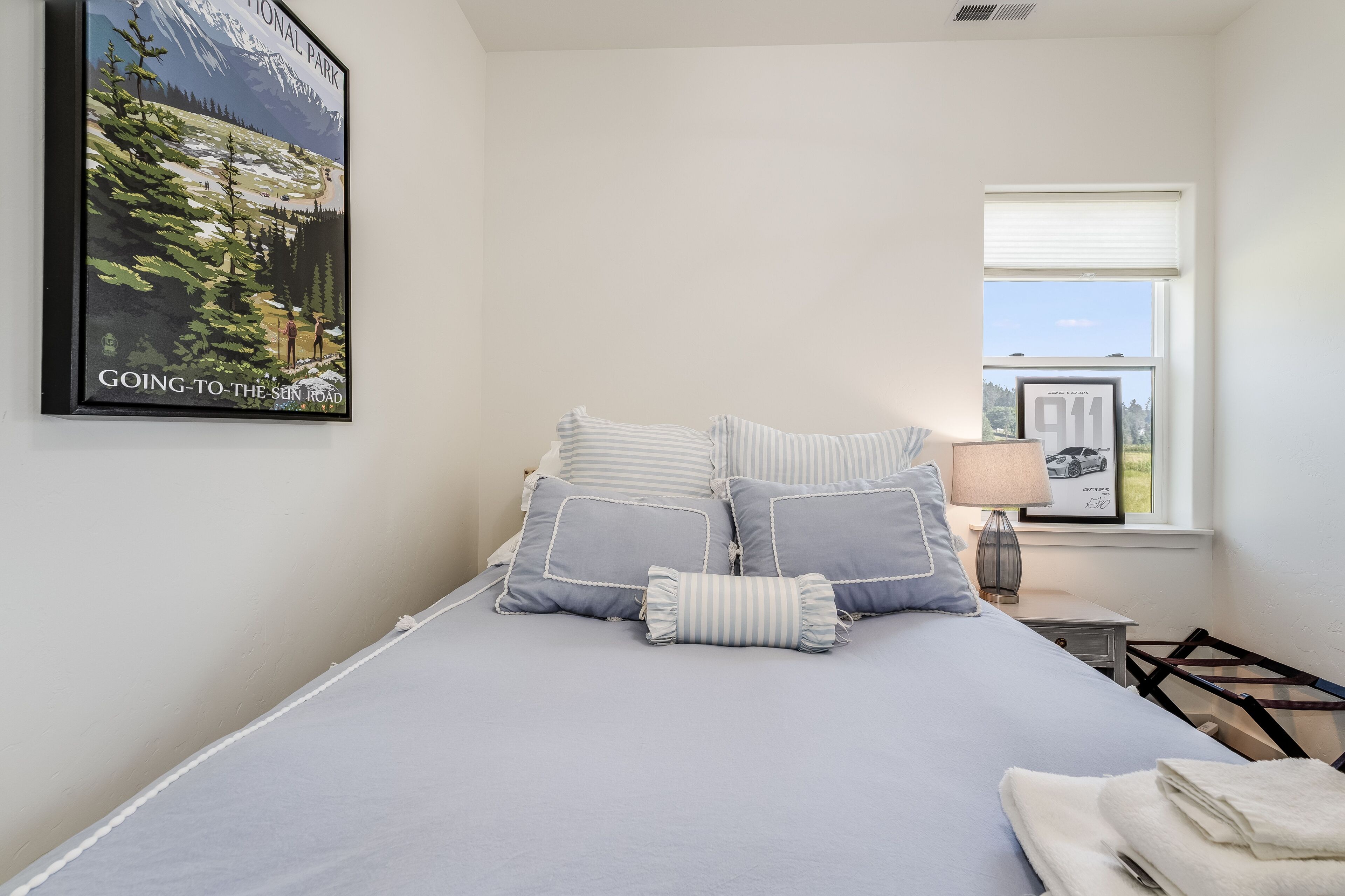 A bedroom with a bed, pillows, a nightstand, a lamp, and a window with a view.
