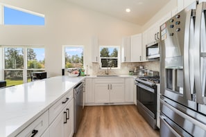 A modern kitchen with white cabinets, stainless steel appliances, and a large island. - New Riverfront Retreat Near Bigfork (Bigfork)