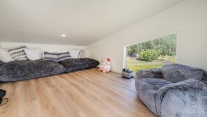 Ein modernes Schlafzimmer im Loft-Stil mit großem Fenster, einem bequemen grauen Sofa und einer dekorativen Hello Kitty Kuscheltierfigur.
