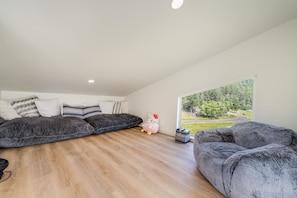 A modern loft bedroom with a large window, a plush gray sofa, and a decorative Hello Kitty plush toy. - New Riverfront Retreat Near Bigfork (Bigfork)