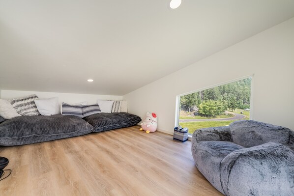 A modern loft bedroom with a large window, a plush gray sofa, and a decorative Hello Kitty plush toy.