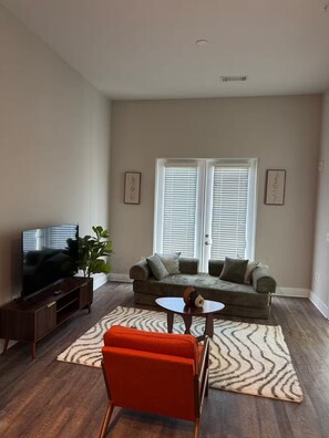 A living room with a sofa, a coffee table, a TV, and a plant. - His Grace Contemporary Living in Truist Park (Atlanta)