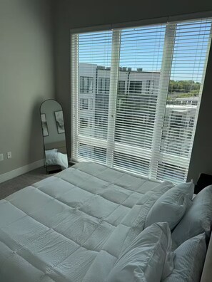 A bedroom with a large bed, a mirror, and a window with blinds. - His Grace Contemporary Living in Truist Park (Atlanta)