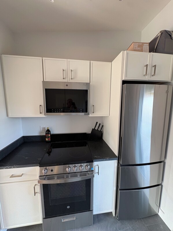 A modern kitchen with white cabinets, a stainless steel refrigerator, a black stove, and a microwave.