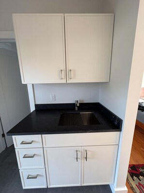 A kitchen with white cabinets, a black countertop, and a stainless steel sink.