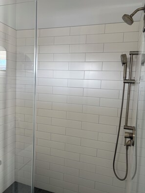 A shower area with a glass door, white tiled walls, and a handheld showerhead.