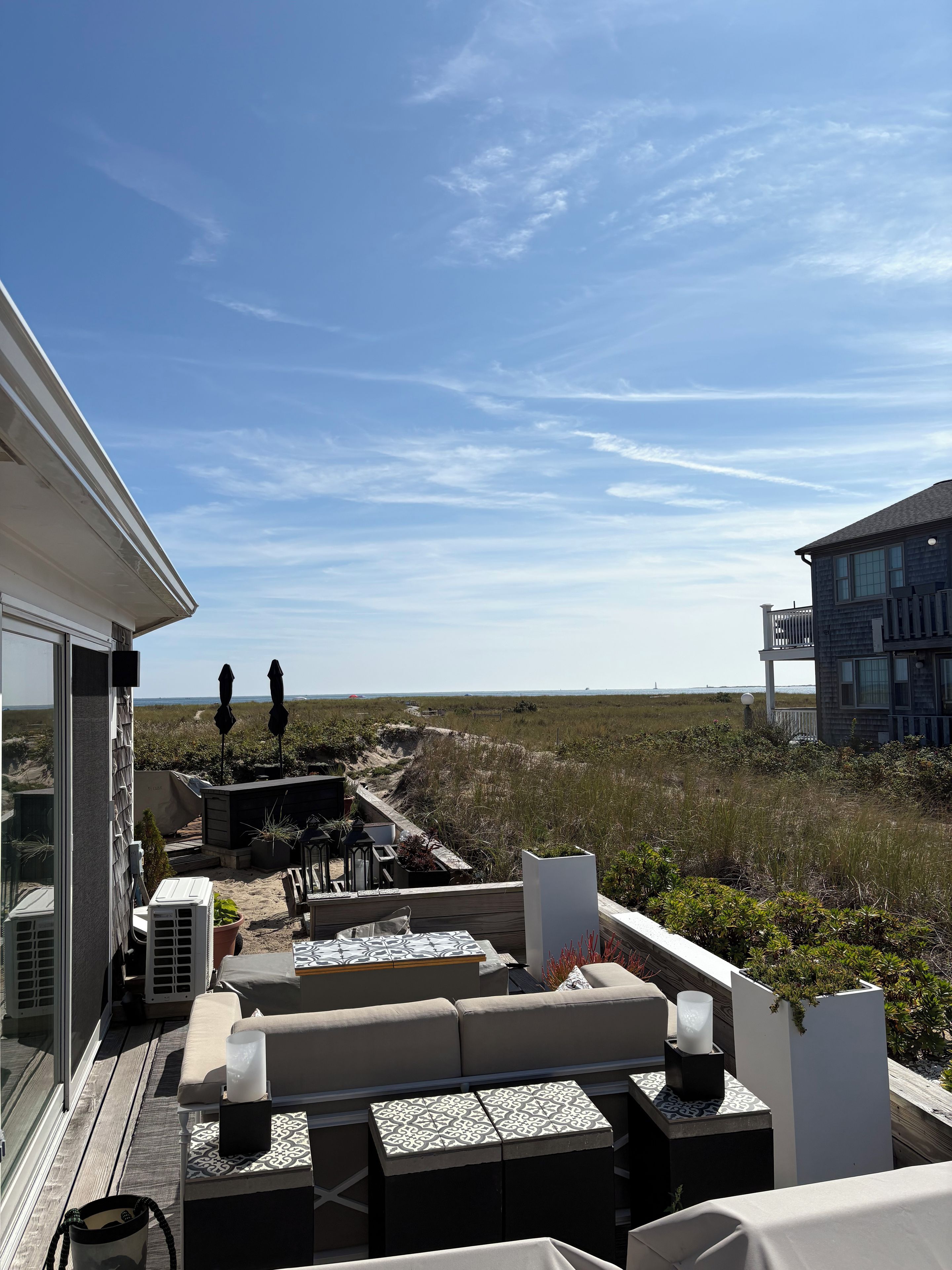 A rooftop terrace with outdoor seating, a view of the beach, and a building in the background.
