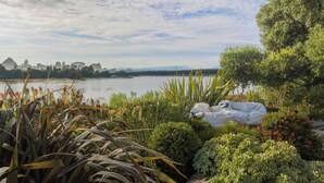 A garden with various plants and a lake in the background. - Estuary Edge in Mapua a luxurious getaway (Māpua)