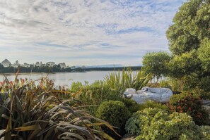 A garden with various plants and a lake in the background. - Estuary Edge in Mapua a luxurious getaway (Māpua)