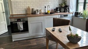 A kitchen with a wooden countertop, a sink, and a stove. There is a dining table with a remote control and a plant on it.