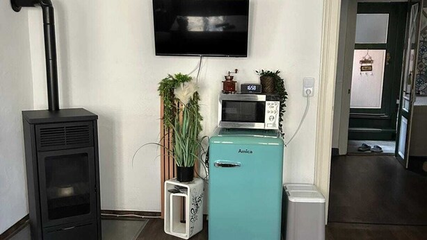 A living room with a black wood-burning stove, a teal refrigerator, a flat-screen TV, and a small potted plant.
