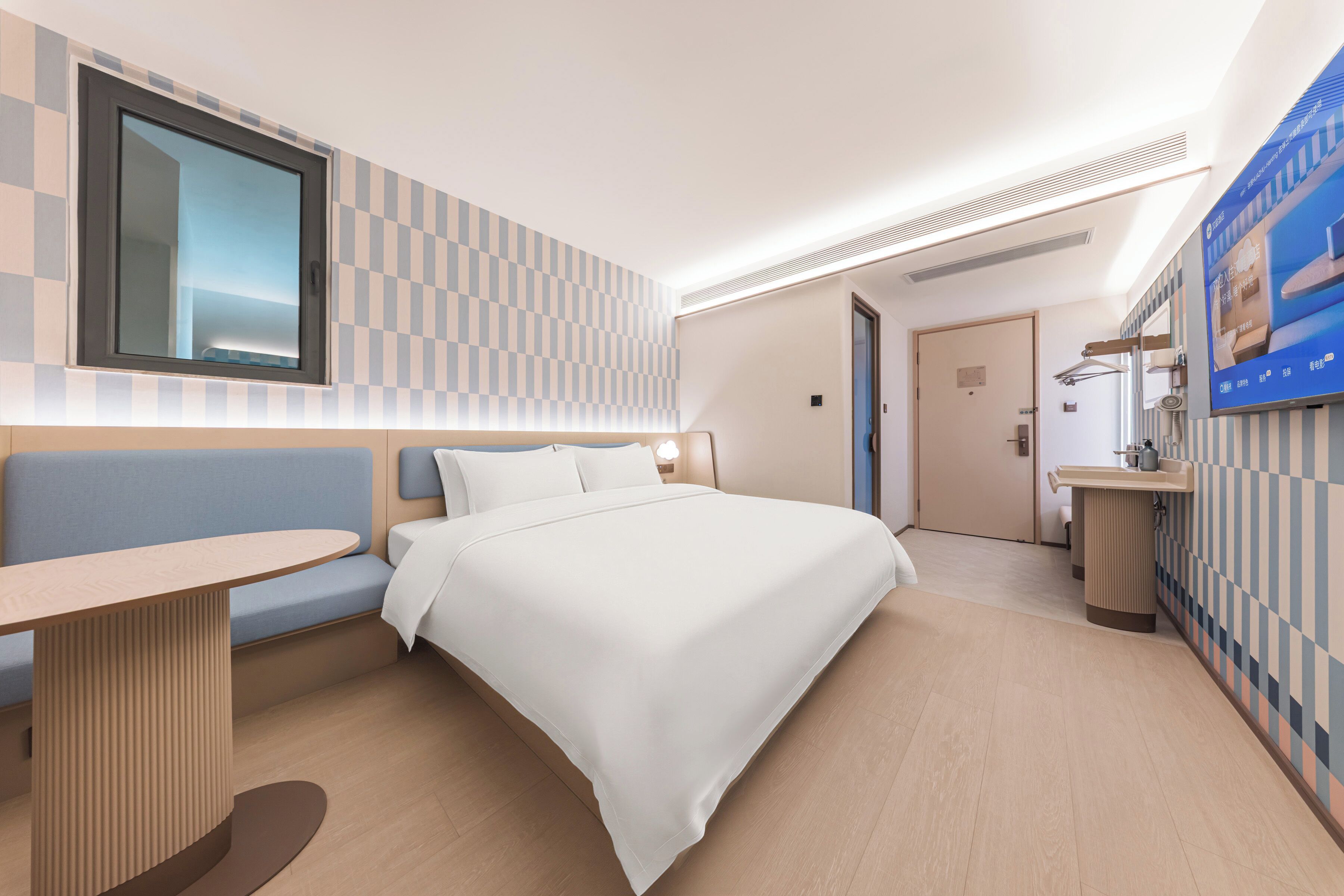 A hotel room with a bed, a seating area, a desk, a window, and a bathroom.
