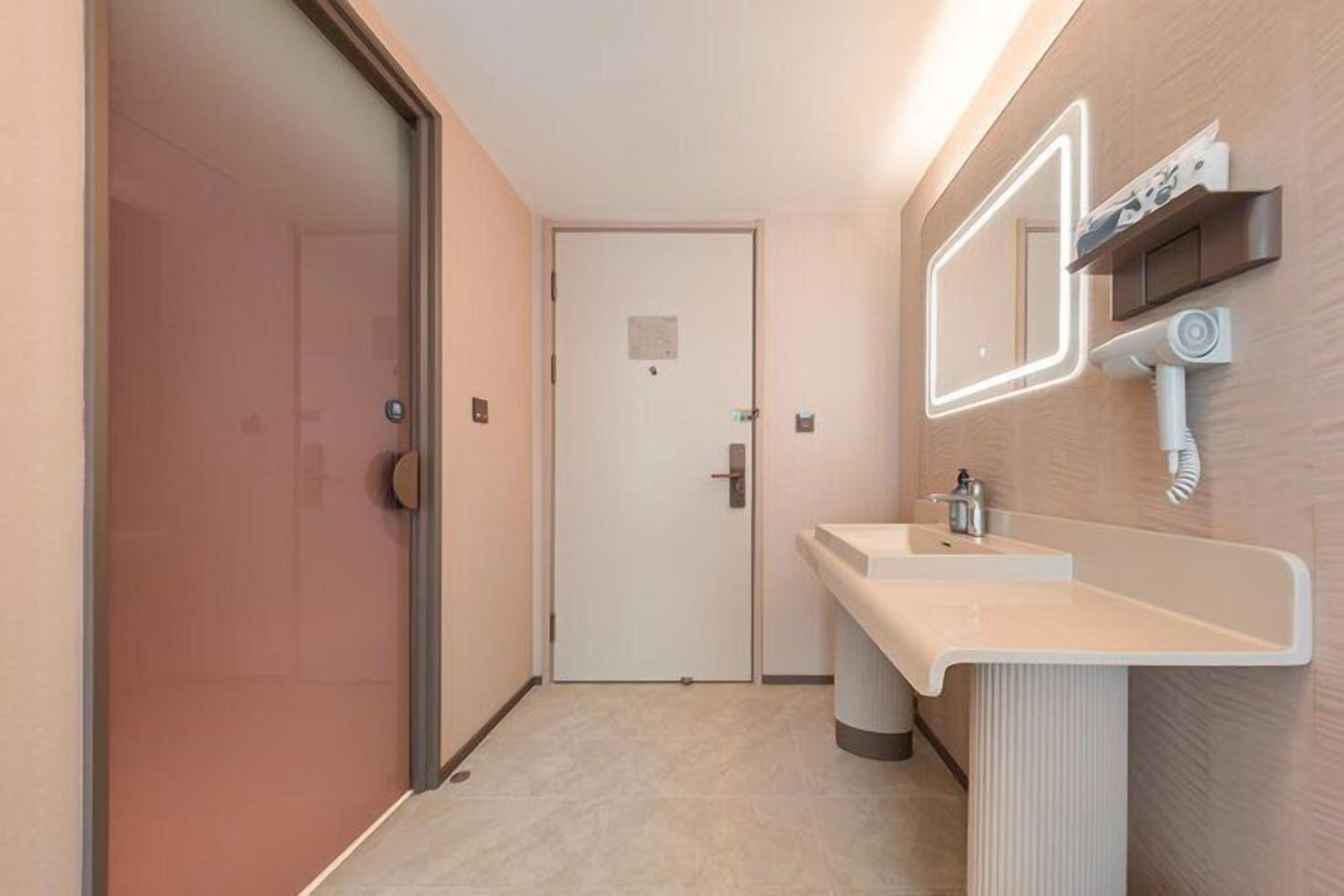 A hotel bathroom with a glass shower door, a sink with a mirror, and a towel dispenser.
