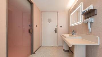 A hotel bathroom with a glass shower door, a sink with a mirror, and a towel dispenser.