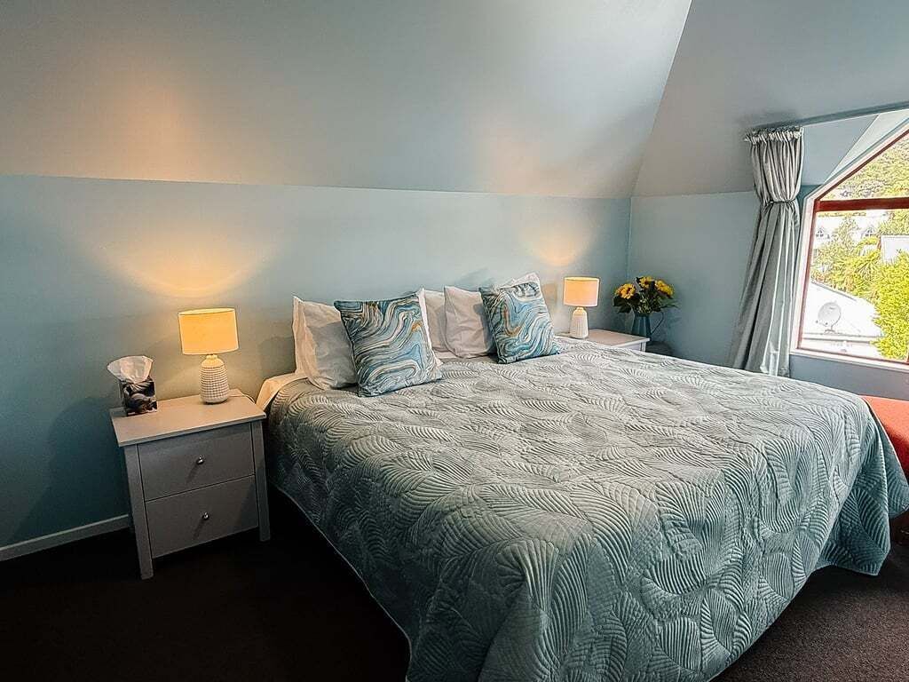 Ein Schlafzimmer mit einem Bett, zwei Nachttischen, Lampen und einem Fenster mit Vorhängen.