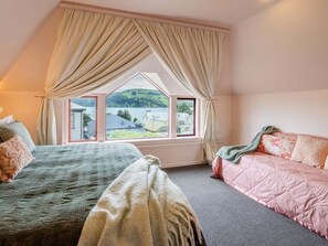 Une chambre avec deux lits, une grande fenêtre avec des rideaux et une vue sur un lac et des collines.