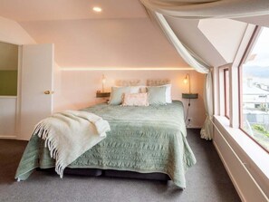 Ein Schlafzimmer mit einem Bett, Nachttischlampen, einem Fenster und Blick ins Freie.