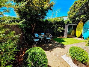 Une terrasse avec une table et des chaises, entourée de verdure et d’une clôture en bois.