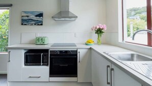 A modern kitchen with a microwave, oven, and toaster, a window with a view, and a vase with flowers on the counter. - Seaview Family Stay Akaroa - Spacious, Sunny & 2 carparks - 2 min walk to waterfront (Akaroa)