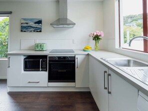 Eine moderne Küche mit Mikrowelle, Backofen und Toaster, einem Fenster mit Aussicht und einer Vase mit Blumen auf der Arbeitsfläche.