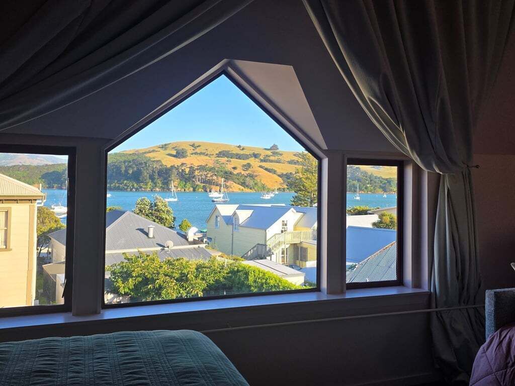 Een kamer met een groot raam, uitzicht op water en heuvels.